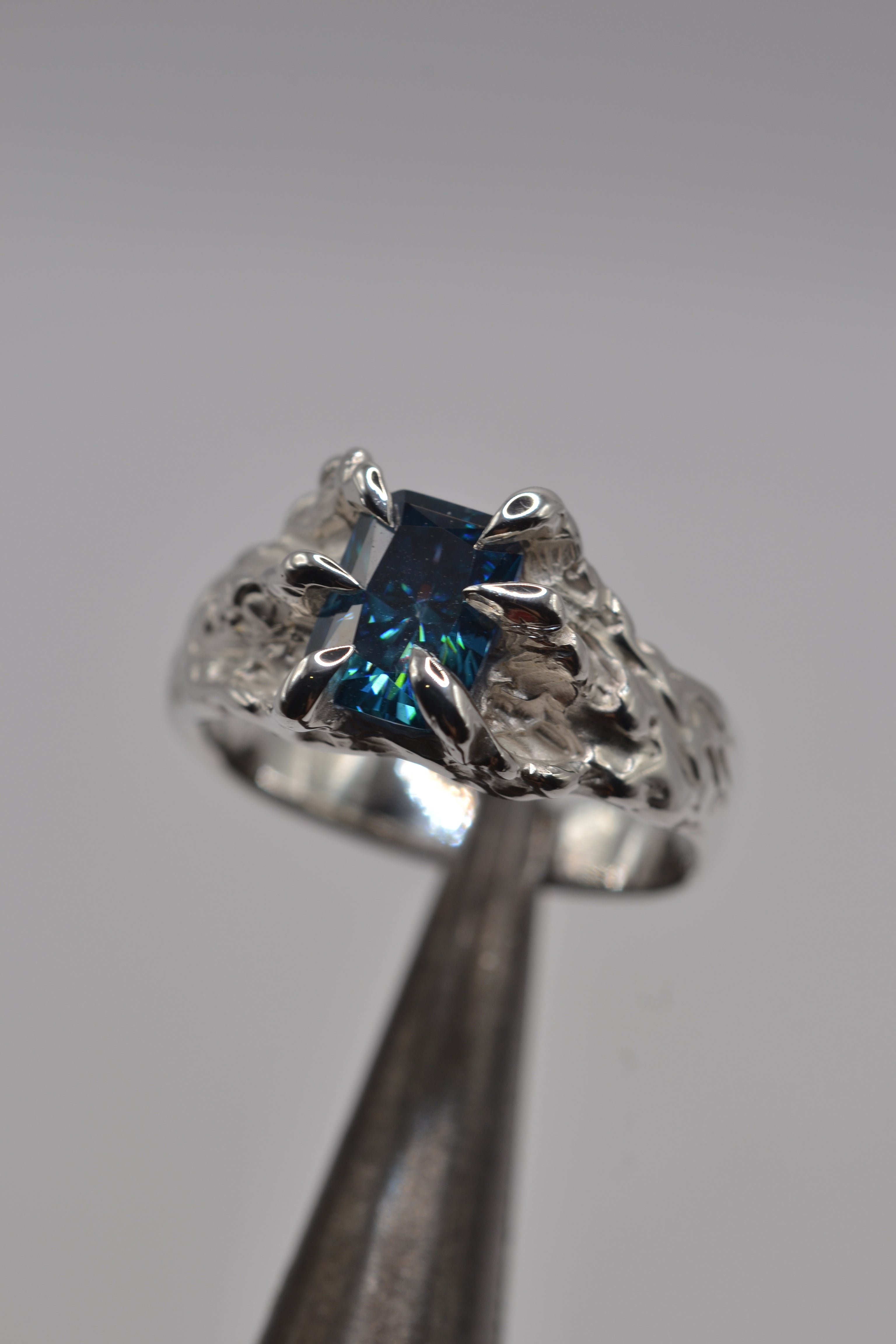 Close up of the Starburst Ring showing radiant cut blue moissanite set within organic molten silver dragon claws handmade using the lost wax technique