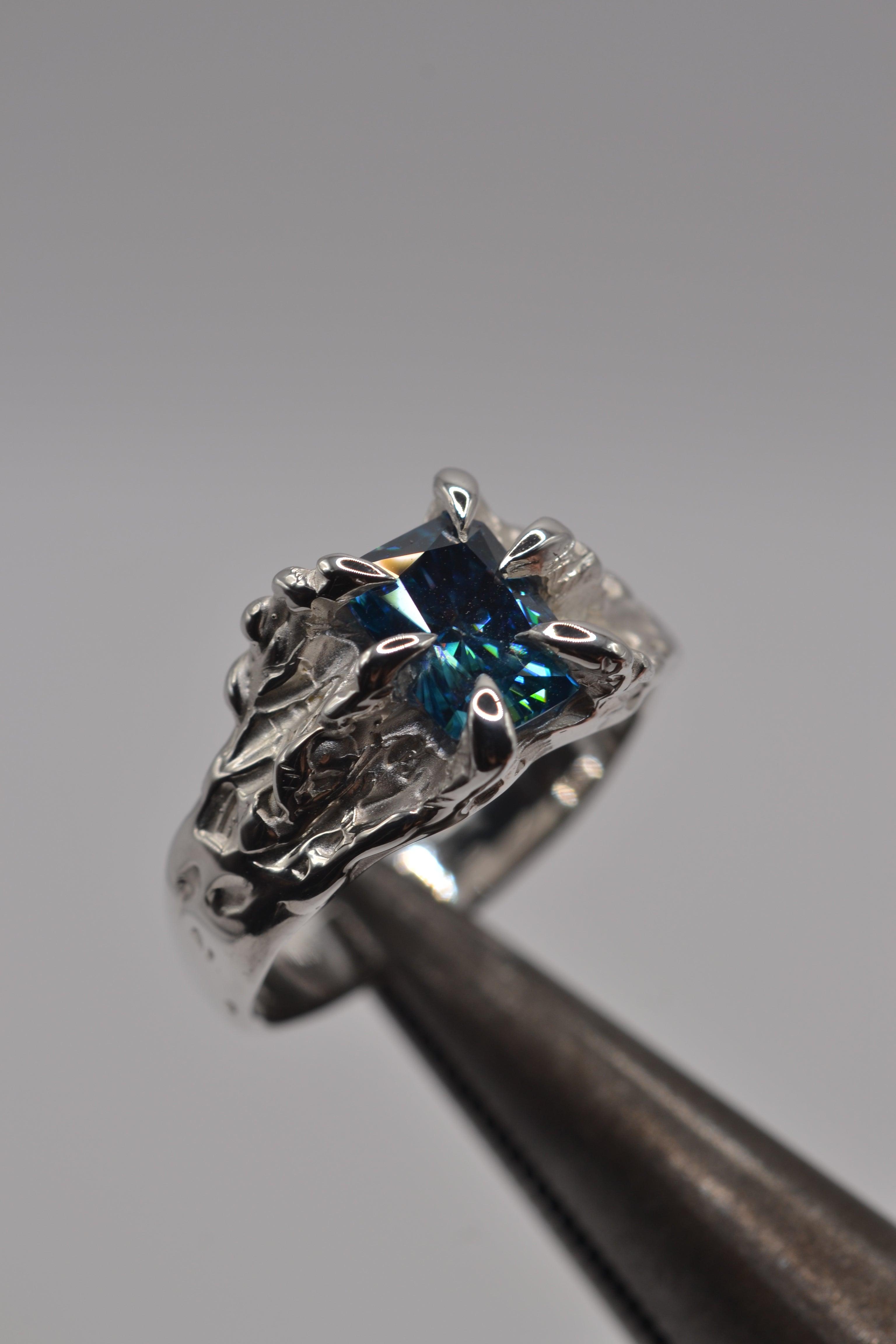 Starburst Ring held in tweezers showing blue moissanite set within organic molten silver claws handmade using the lost wax casting technique