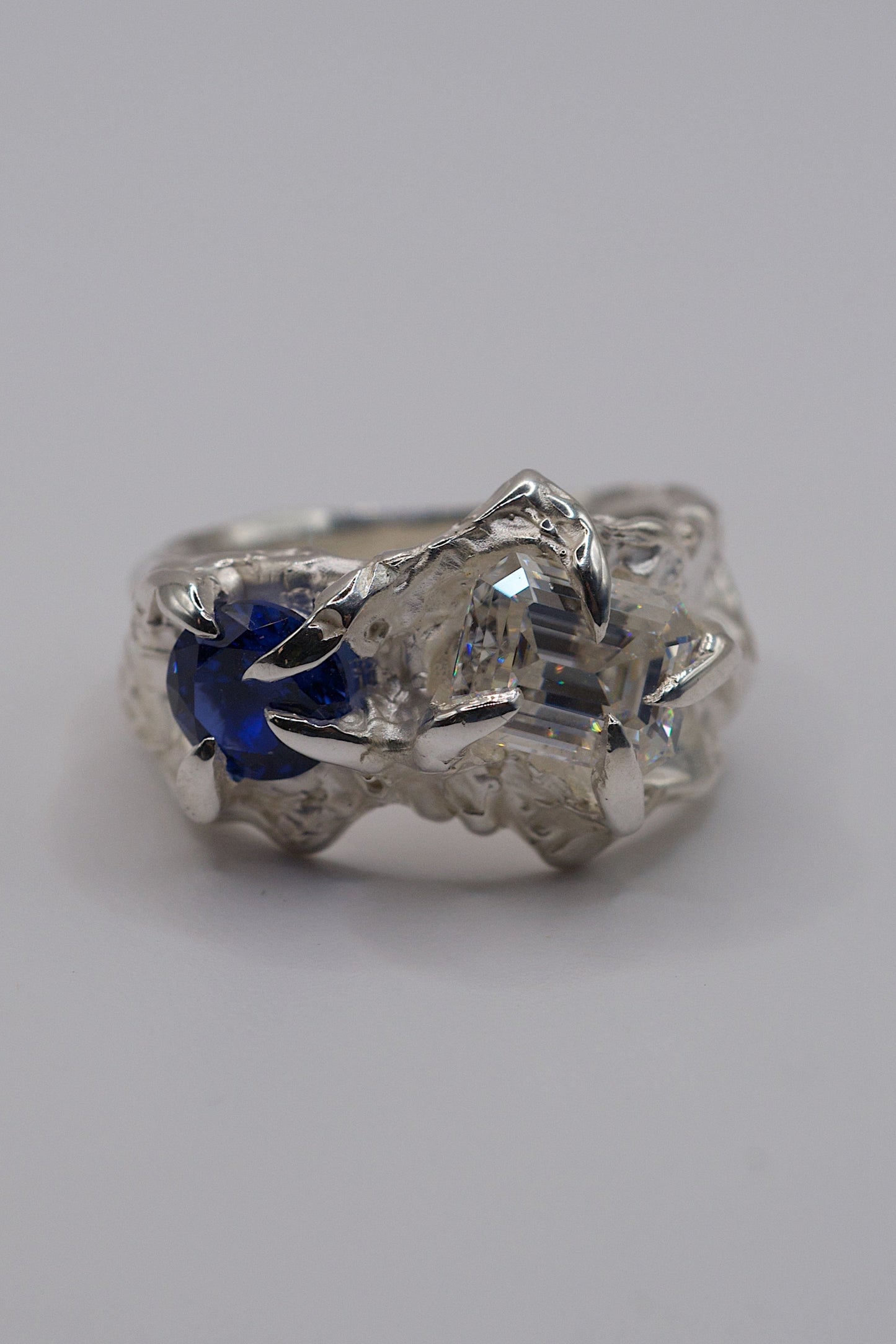 Handmade organic sterling silver ring with heavily textured details featuring a blue natural round sapphire and clear white moissanite handmade by lost wax build-up technique.