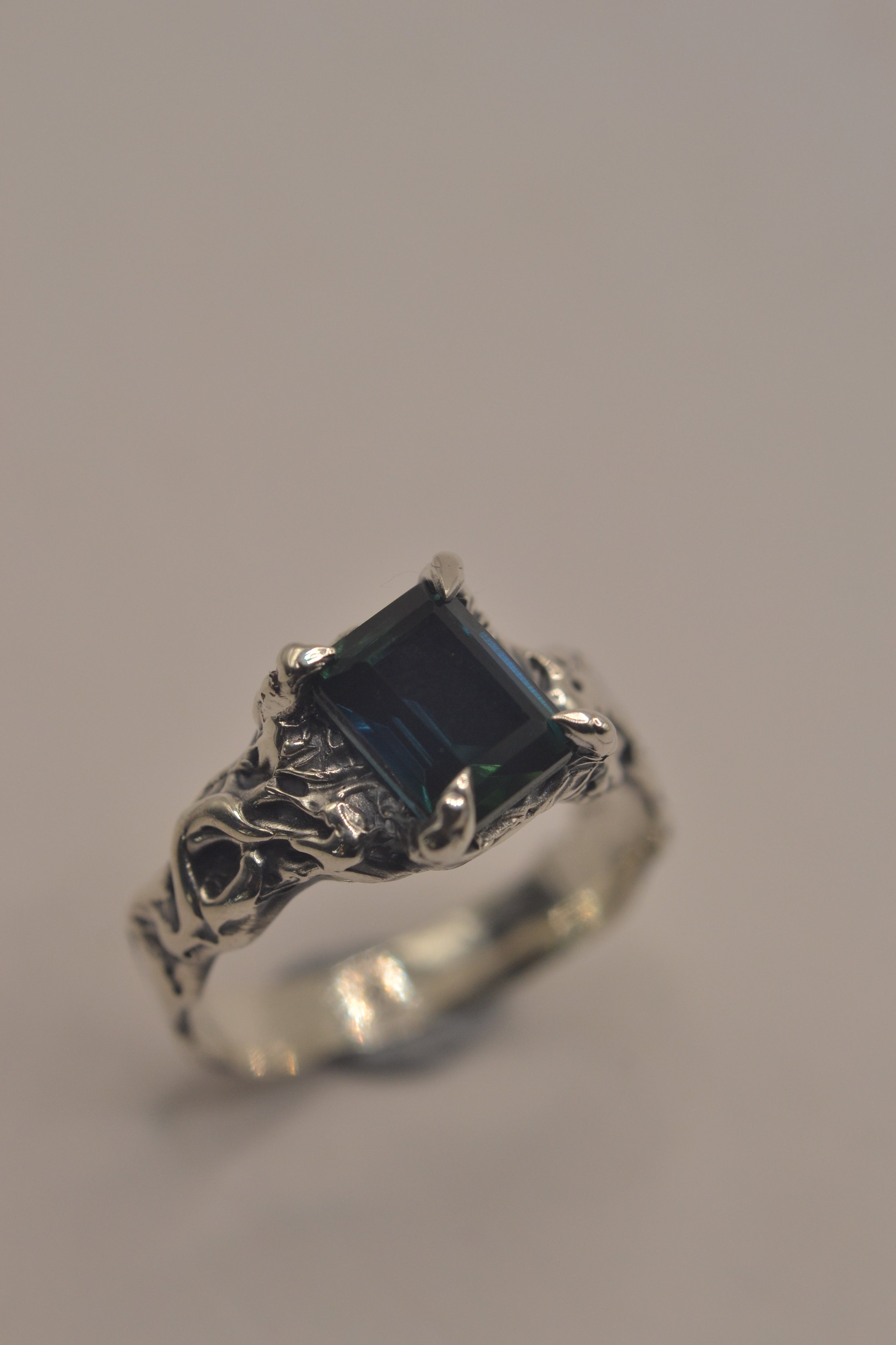 Another angle of the Twilight Ring showing teal emerald cut sapphire within heavily textured darkened sterling silver lost wax cast