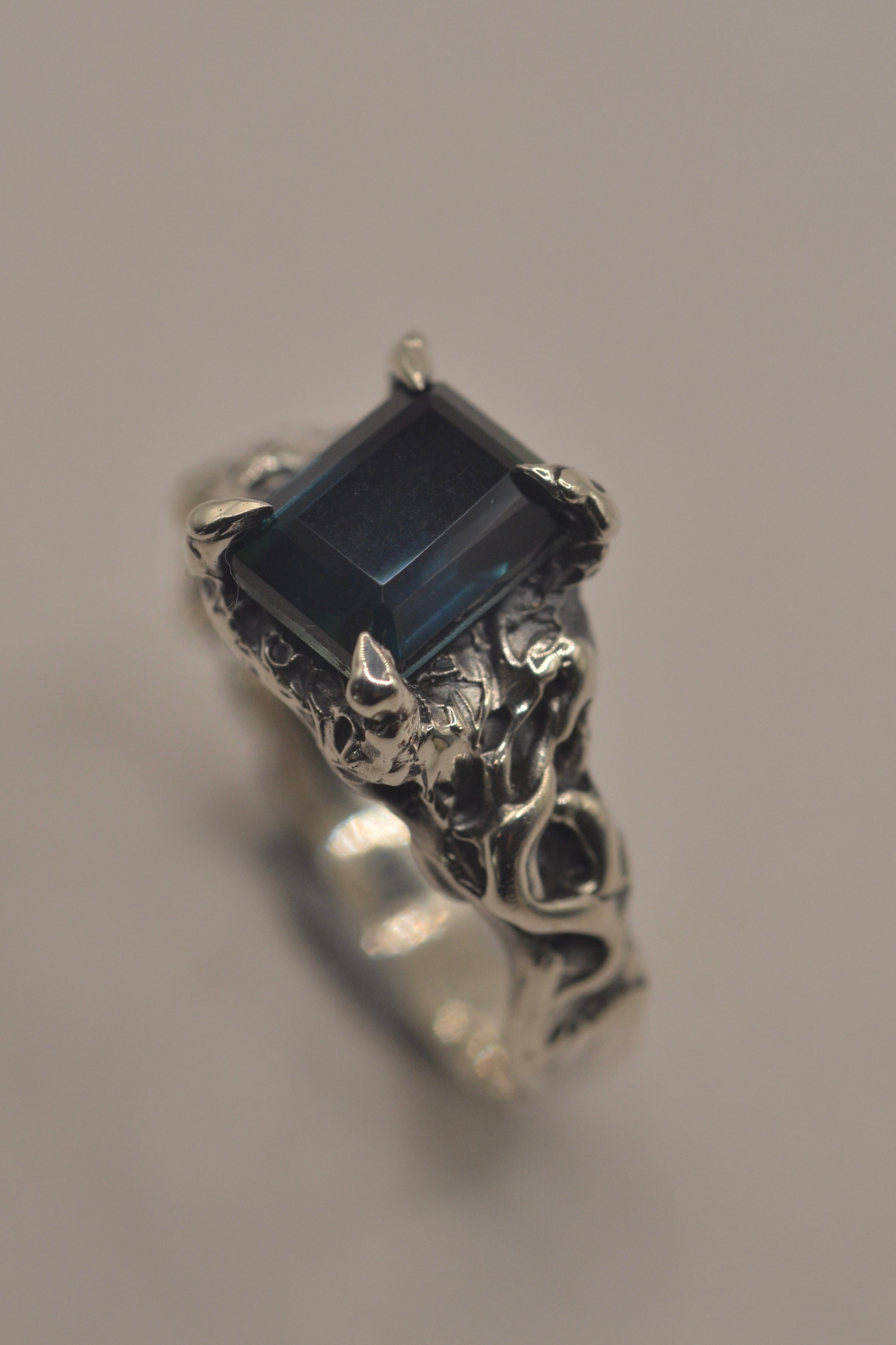 Side angle of the Twilight Ring showing teal emerald cut sapphire within heavily textured darkened sterling silver handmade using the lost wax technique