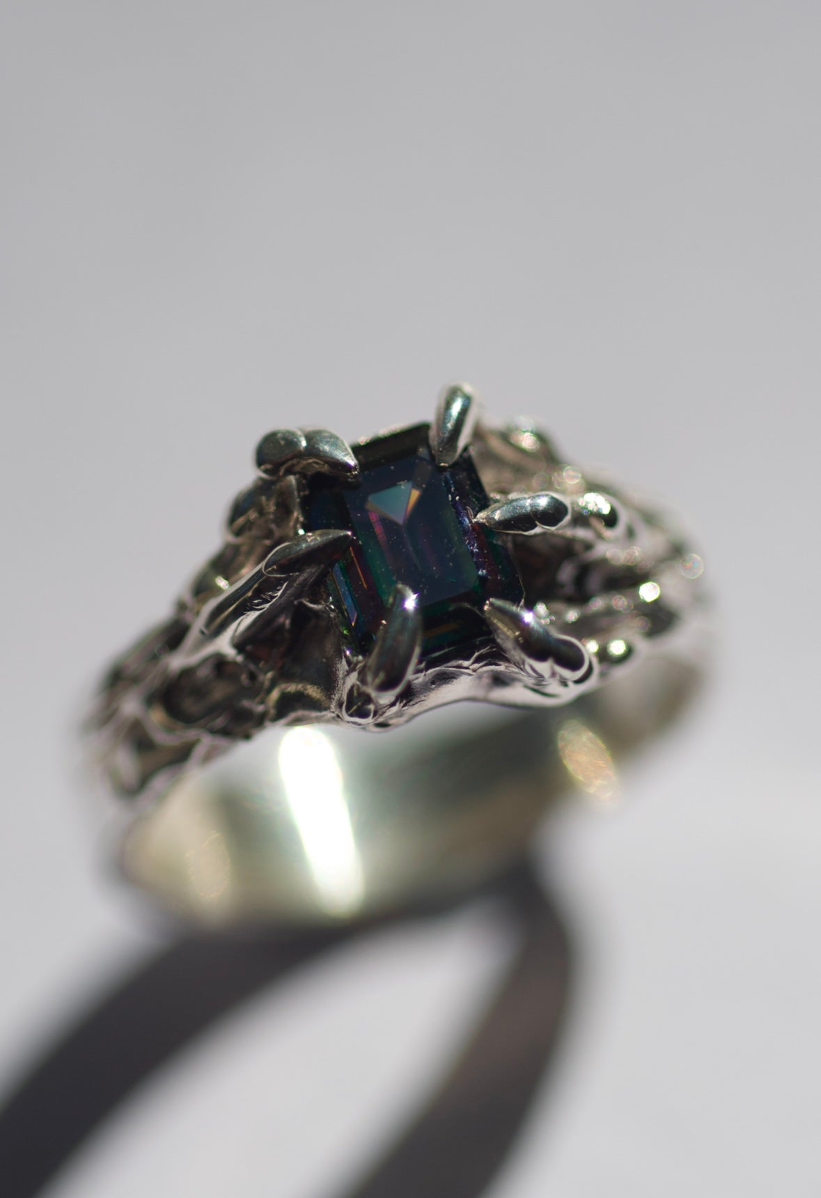 Close up of the Violet Ring showing vibrant rainbow emerald cut moissanite within sharp molten sterling silver claws handmade using the lost wax technique