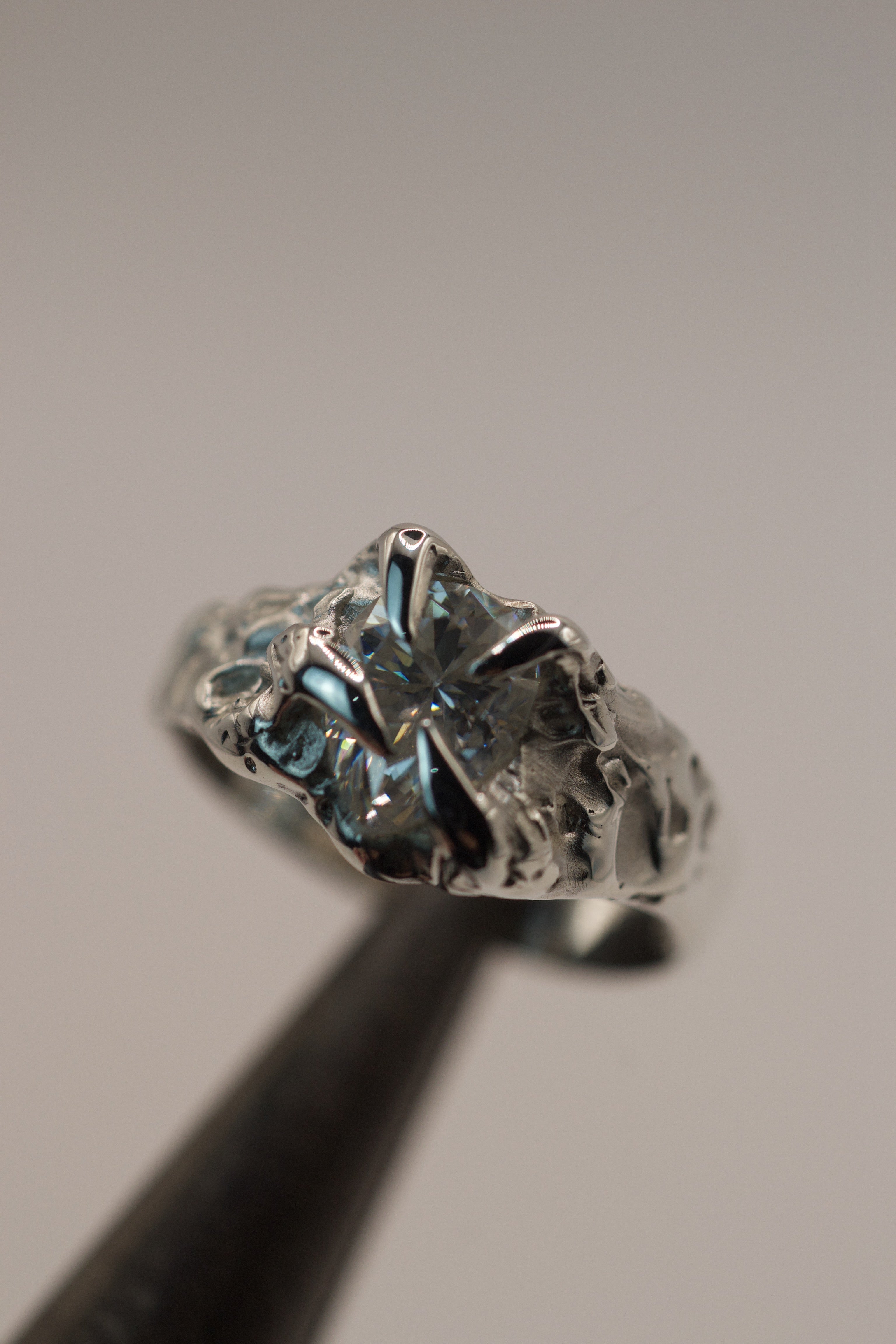 Side angle of the Winter Ring held in tweezers showing organic molten recycled sterling silver band and pear cut moissanite setting